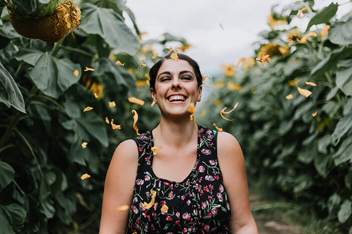 femme heureuse souriante entourée de pétales de fleurs dans un champ
