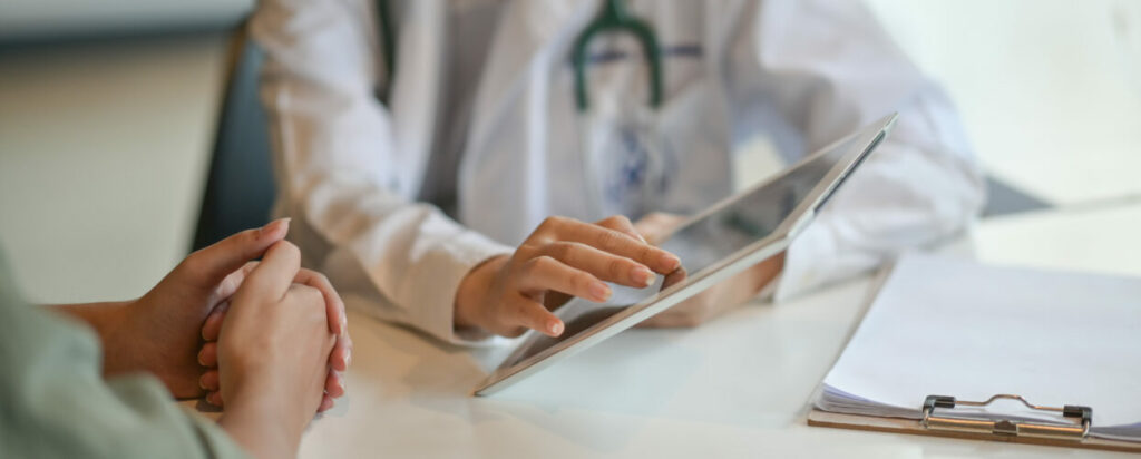 Aufnahme eines Arztes, der einem Patienten einige Informationen auf einem digitalen Tablet zeigt
