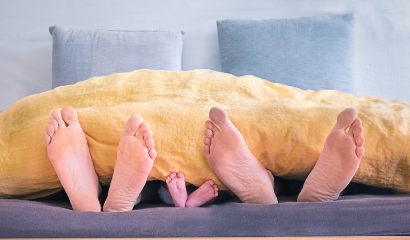 Familie im Bett, die Fuesse ragen aus der Decke heraus